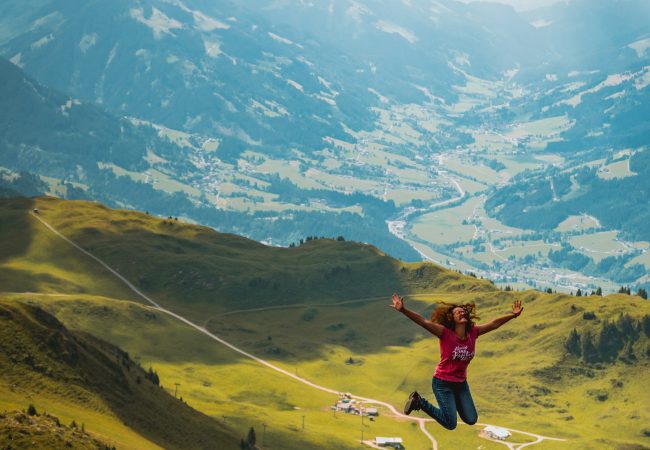 woman jumping on hill during daytime