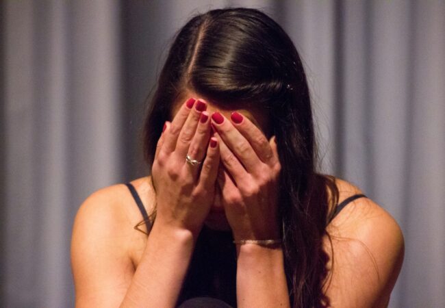 woman in black tank top covering her face with her hands